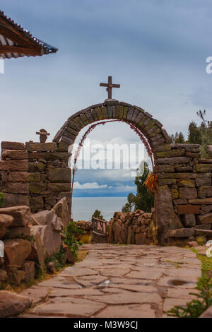 Arco in pietra all entrata del villaggio in un giorno nuvoloso, Taquile Island, il lago Titicaca, Perù Foto Stock