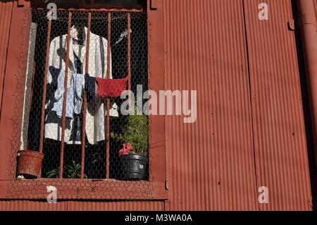 Una camicia bianca e altri vestiti di essiccazione al sole nella finestra di una casa fatta dal rosso di ferro ondulato Foto Stock