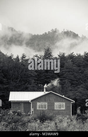 Una casa in legno con fumo proveniente dal camino contro un Bosco nebbioso sfondo Foto Stock