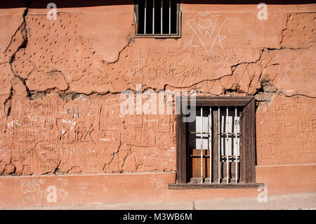 Una parete arancione contrassegnato con fori, graffiti e incisioni con un chiuse la finestra in legno in Valle de Elqui, Cile Foto Stock