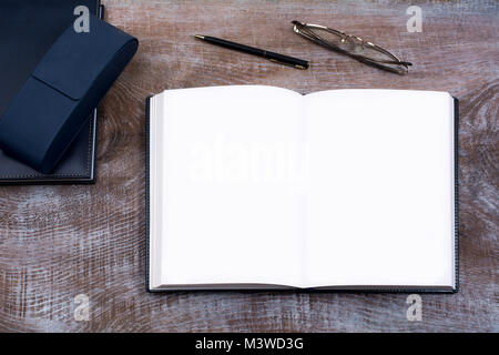 Mockup di aprire il notebook con pagine vuote, penna, occhiali, navy blue case e prodotti lattiero caseari sul tavolo di legno Foto Stock