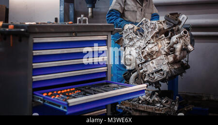 Revisionare la riparazione. Il giovane meccanico automatico smantella il motore di contrasto per la diagnosi e la riparazione presso lo stand in officina. Foto Stock