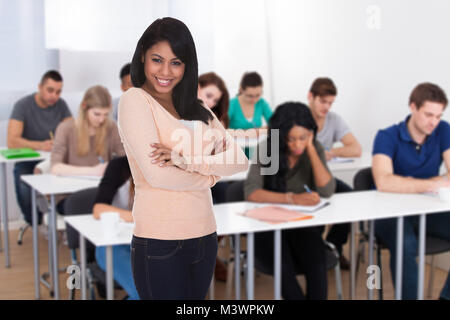 Ritratto di un felice studente con le mani giunte in piedi in aula Foto Stock