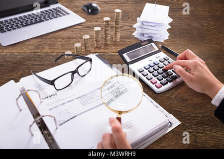 Close-up di un imprenditore la mano analizzando Bill con lente di ingrandimento a Workplace Foto Stock