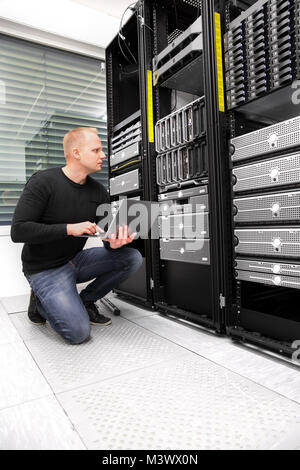 Consulente maschio utilizzando computer portatile mentre il monitoraggio dei server in Datacen Foto Stock