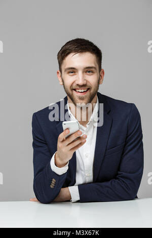 Il concetto di business - Ritratto bello bello Happy business man in tuta la riproduzione telefono mobili e sorridente con notebook a lavorare in ufficio. Sfondo bianco. Foto Stock