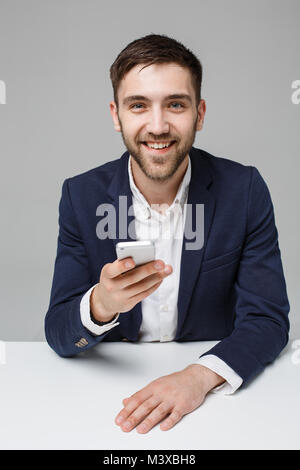 Il concetto di business - Ritratto bello bello Happy business man in tuta la riproduzione telefono mobili e sorridente con notebook a lavorare in ufficio. Sfondo bianco. Foto Stock