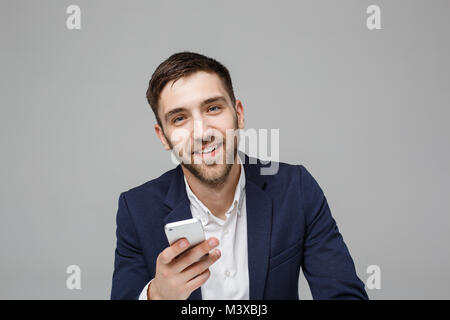 Il concetto di business - Ritratto bello bello Happy business man in tuta la riproduzione telefono mobili e sorridente con notebook a lavorare in ufficio. Sfondo bianco. Foto Stock