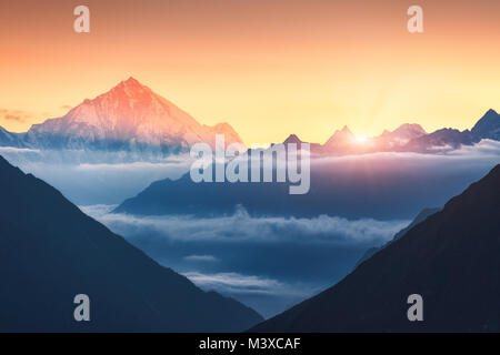 Maestoso scenario di sagome delle montagne e nuvole basse a sunrise colorati in Nepal. Paesaggio con cime innevate delle montagne, bellissimo cielo e giallo Foto Stock