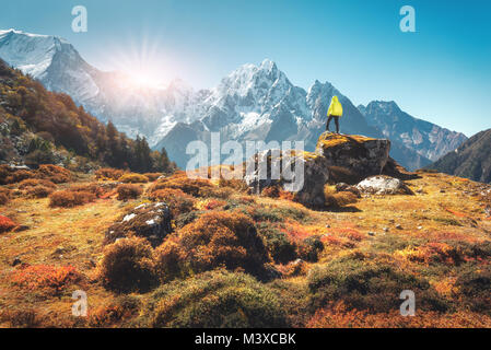 Uomo in piedi sulla pietra e cercando su incredibili montagne himalayane al tramonto. Paesaggio con traveler, alte rocce con vette innevate, piante, foresta io Foto Stock