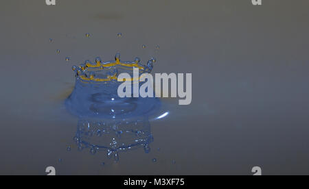 Caduta impattante nel liquido blu arancione con corona blu Foto Stock