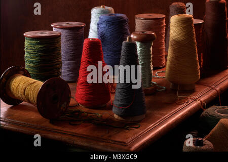 Più steli di tessitura con cotone o lana thread su di essi. Colore verticale fotografia scattata in un studio impostazione con illuminazione drammatica. Terriccio scuro Foto Stock