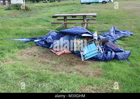 Abandonned, crollato, blu tenda, sacco a pelo e camping sedile accanto al legno un tavolo da picnic sul prato verde. Camping disater. Foto Stock