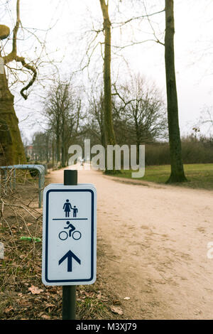 Segno che indica la direzione della bicicletta e percorso a piedi in un parco con alberi sfocata sullo sfondo Foto Stock