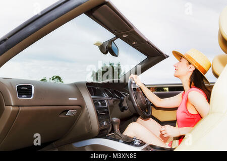 Signora giovane guidatore seduto nel lusso moderno autovettura convertibile con capote in giù sotto il cielo aperto sterzo e guida alla libertà. Foto Stock