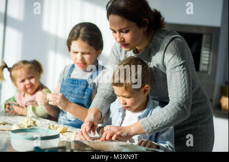 Madre insegna ai figli come cucinare. Due ragazze e il ragazzo molto provare. I loro volti in farina, pasta ha bloccato per le mani. Foto Stock