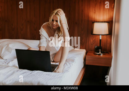 Ritratto di un sorridente casual giovane donna utilizzando laptop nel letto di casa Foto Stock