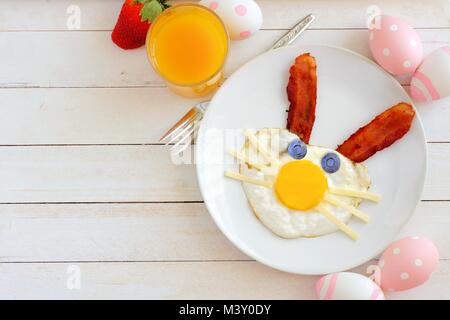 Colazione di pasqua con cute bunny faccia fatta di uova e bacon. Tabella scena, sopra vista su un bianco sullo sfondo di legno. Foto Stock