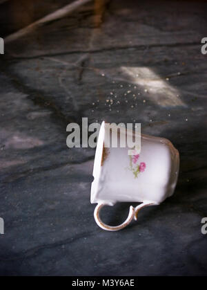 Ancora la vita di porcellana antica francese tazza di caffè sul suo lato sul piano di marmo con granuli di zucchero in background Foto Stock