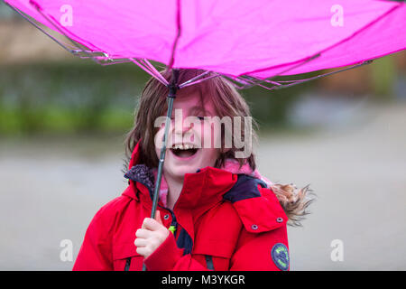 Ashford, Kent, Regno Unito. Xiii Febbraio, 2018. Un bambino di 8 anni bambino vestito con una giacca rossa gioca sotto la pioggia con un ombrello rosa che ha ripiegato stesso dentro e fuori. Credito Foto: immagini di PAL /Alamy Live News Foto Stock