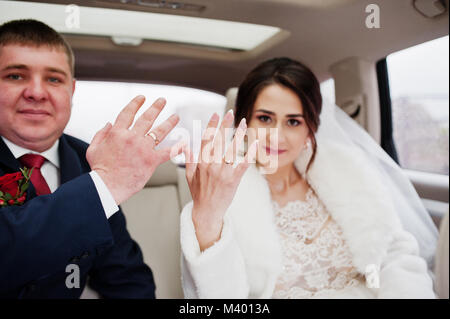 Coppie in viaggio di nozze è seduto in macchina e mostrare i loro anelli sul loro giorno delle nozze. Foto Stock