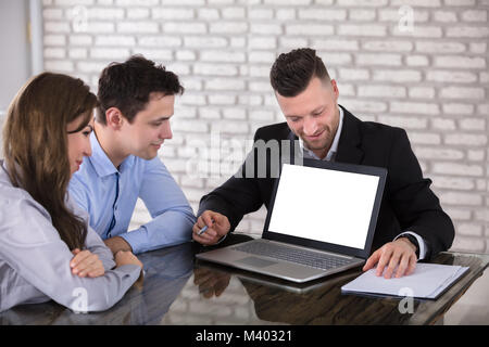 Imprenditore sorridente mostra portatile al giovane sulla scrivania in ufficio Foto Stock