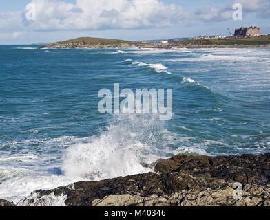 Preso mentre si cammina intorno Fistral Beach, onde che si infrangono sulle rocce con il Headland hotel e Heurs capanna in background. Foto Stock