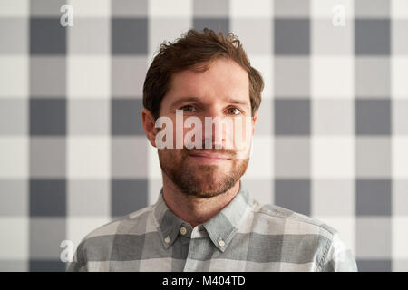 Sorridente giovane uomo che indossa una camicia matching il suo sfondo a scacchi Foto Stock