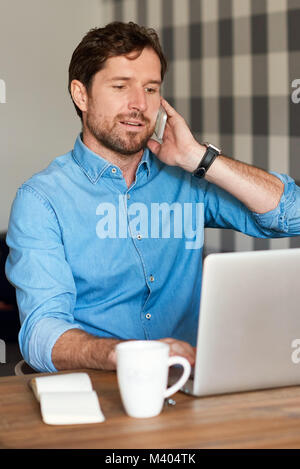 Uomo bello parlare su un telefono cellulare e di lavoro on-line Foto Stock