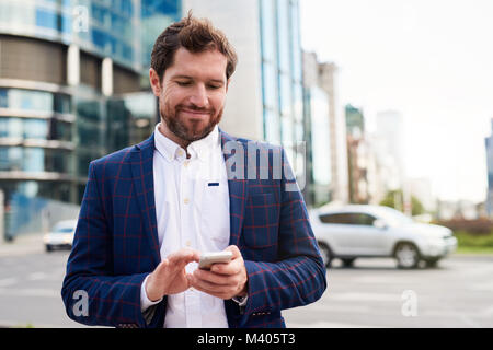 Imprenditore sorridente invio di messaggi di testo mentre in piedi in città Foto Stock