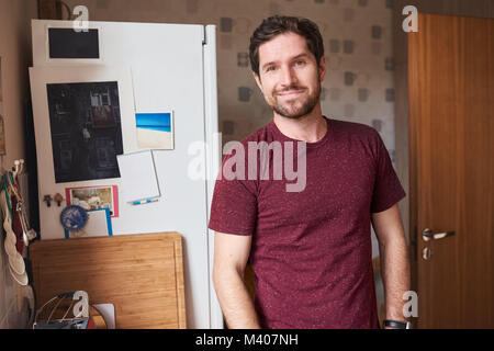 Sorridente giovane uomo in piedi nella sua cucina a casa Foto Stock