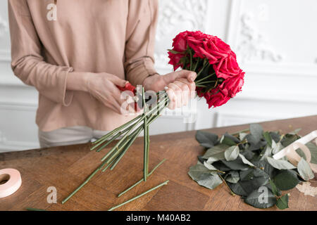 Giovane donna fioraio disponendo le piante nel negozio di fiori. Persone, business vendita fiorai e concetto. Bouquet di rose rosse Foto Stock