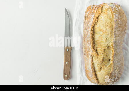 Pane appena sfornato Artigianale il pane rustico focaccia sulla biancheria da letto bianca asciugamano con coltello sulla trama del piano portapaziente in calcestruzzo. Giapponese minimalista in stile autentico. Vite Foto Stock