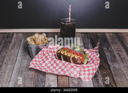 Gourmet hot dog con patatine e drink in un cestello con gingham igienico. Il piano portapaziente, vista frontale. Foto Stock