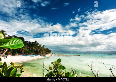 Spiaggia di sabbia bianca, Boracay, Filippine, spiaggia tropicale con palme, cielo blu con nuvole, lascia in primo piano. Ampio angolo Foto Stock