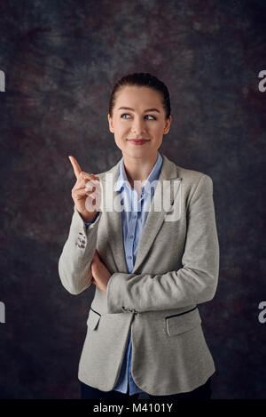 Smart sorridente giovane professionista o business donna puntando il dito in aria con un sorriso soddisfatto in quanto essa trova una soluzione ad un problema o si pensa Foto Stock