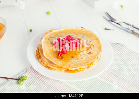 Frittelle sottili con rosse bacche Ribes sul bianco servito un tavolo di legno. Stile rustico. Tradizionale per il pancake russo settimana (Maslenitsa). Selectiv Foto Stock