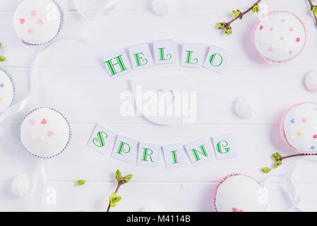 Vista superiore della composizione Ciao molla scritte, rami con giovani germogli di verde, pasqua tortine, il merengue, caramelle, artigianato bird figura su woo Foto Stock