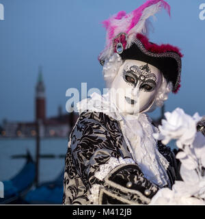 Maschio goer di carnevale in costume tradizionale e la maschera in piedi con la schiena al Canal Grande e gondole e San Giorgio in background Foto Stock