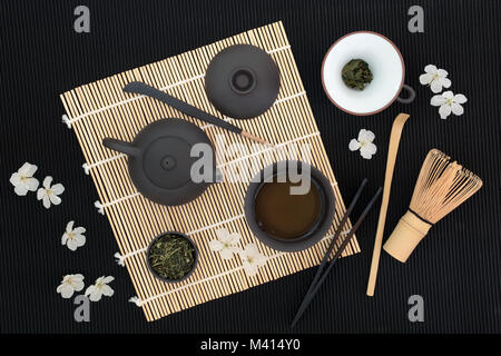 Sencha sukiygu makoto giapponese del tè con teiera e tazza, foglie secche, frusta, filtro, scoop, stick agitatore, tenaglie e la primavera sbocciano i fiori sul bambù e b Foto Stock