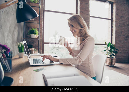 Concetto di avere un posto di lavoro a casa. Profilo lato a metà di fronte foto di felice allegro sorridente Excited donna a bere caffè e la digitazione di una lettera sul co Foto Stock