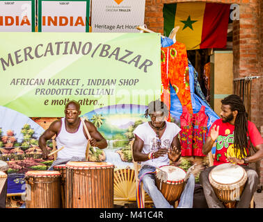 Un gruppo di musicisti africani gioca con i tamburi africani e cantare canzoni di fronte ad un mercato tradizionale africano Foto Stock