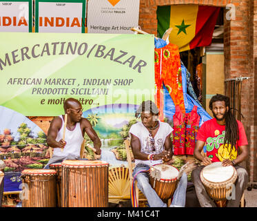 Un gruppo di musicisti africani gioca con i tamburi africani e cantare canzoni di fronte ad un mercato tradizionale africano Foto Stock