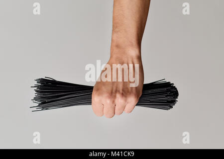 Primo piano di un giovane uomo caucasico con un mazzetto di crudo spaghetti al nero nella sua mano contro un fondo bianco Foto Stock