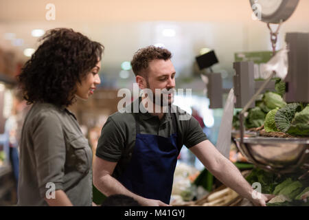 Assistente di negozio in negozio di alimentari aiutando shopper Foto Stock