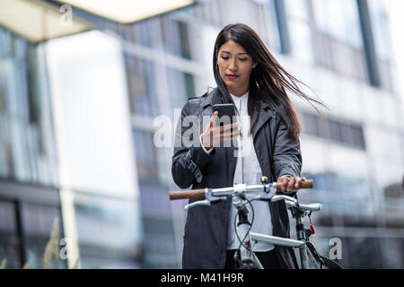 Imprenditrice escursioni in bicicletta al lavoro utilizza lo smartphone Foto Stock