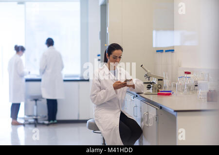 Donna scienziato utilizza lo smartphone in laboratorio Foto Stock