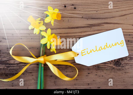 Etichetta con testo in inglese significa Einladung invito. Giallo sole di primavera o Narciso Daffodil con nastro. Invecchiato, botte rustico sfondo. Saluto Ca Foto Stock