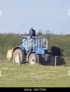 Il trattore taglio di siepi una siepe su terreni agricoli in febbraio, REGNO UNITO Foto Stock