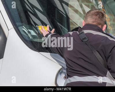 Parcheggio operaio mettendo a disposizione un parcheggio ticket nota penalità sul finestrino di un'automobile in Inghilterra, Regno Unito. Parcheggio enforcement officer. Foto Stock